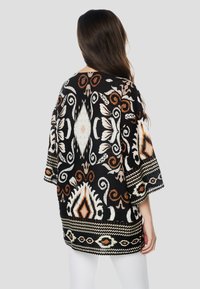 Top negru cu modele florale şi geometrice în alb, portocaliu şi bej. Croială lejeră cu mâneci largi şi țesătură texturată.