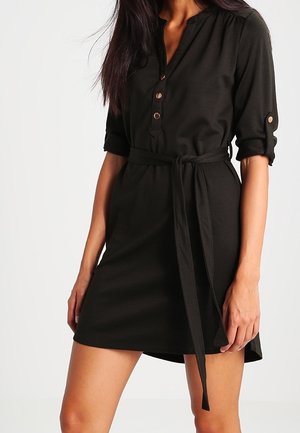 Czarna sukienka koszulowa z krótkim rękawem, z zapięciem na guziki, pasek w talii i lekko rozszerzaną spódnicą. Wykonana z miękkiego, lekkiego materiału.