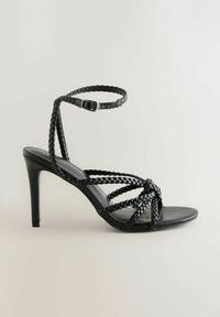 Sandali neri con tacco alto caratterizzati da cinturini intrecciati, design aperto sulla punta e fibbia alla caviglia regolabile. Materiale in pelle liscia con una finitura elegante.