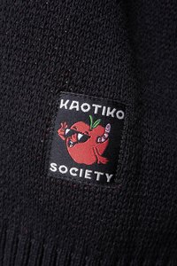 Crna pleta tkanina s veselom izvezenom naljepnicom koja prikazuje karikaturu, crvenu jabuku sa sunčanim naočalama i tekst "KAOTIKO SOCIETY."