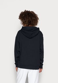 Sudadera negra de gran tamaño con capucha ajustable, puños y dobladillo acanalados, fabricada en un material suave, exhibida desde la parte posterior sobre un fondo claro.