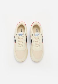 Beige sneakers med røde og marineblå aksenter. Mesh og glatt tekstiloverdel, rund tå og flate lisser. Branding på tungen. Gummisåle.