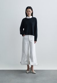 Maglione nero in maglia con orlo a coste, abbinato a jeans bianchi a gamba larga con risvolti. Calzature: scarpe con tacco alto e texture.