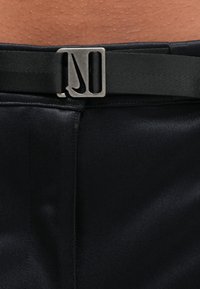 Črni platnen pas z mat srebrno kovinsko zaponko z logotipom Nike. Dizajn vključuje gladko teksturo in trdno izdelavo.