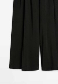 Schwarze Hosen mit weitem Bein, lockerem Schnitt und geradem Saum, dargestellt vor weißem Hintergrund.