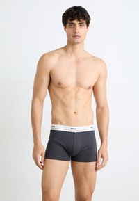 Graue Boxer-Shorts mit einem weißen Bund. Der Bund ist mit dem "BOSS"-Logo versehen. Glatte Textur, körperbetonter Schnitt und mittellange Beine.