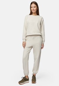 Kremowa bluza i dopasowane dresy z miękkiego materiału. Rybaczane mankiety i pas. Brązowe sneakersy na sznurówki dopełniają zestaw.