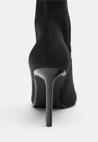 Crne visokotlačne gležnjače od rastezljive tkanine s šiljastim prstima, uskim stiletto potplatom i bočnim patentnim zatvaračem.