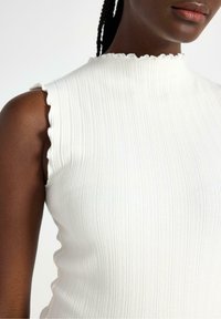 Top bianco a righe senza maniche con scollatura ondulata, caratterizzato da un design aderente e una texture morbida. Nessun motivo o dettaglio visibile.