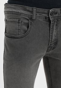 Vaqueros de mezclilla gris con un ajuste slim, que cuentan con un diseño clásico de cinco bolsillos, cierre con botón en la parte superior y detalles de costura sutiles.