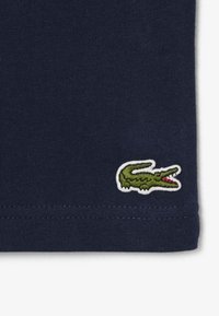 Tissu bleu marine avec un petit logo crocodile vert brodé près du bord inférieur.