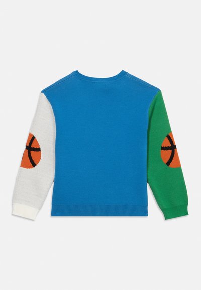 Μπλε πουλόβερ με ένα λευκό και ένα πράσινο μανίκι, με πορτοκαλί μπαλονοπάτσες σε κάθε αγκώνα.