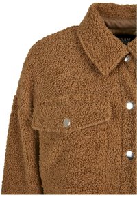 Brun fleece skjortejakke med en teksturert overflate, fold-down krage og sølvfargede trykknapper på fronten og brystlommen.