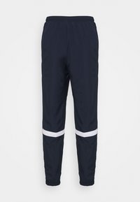 Marina blå sportbyxor med vita horisontella ränder ovanför knäna, elastisk midja och elastiska muddar vid anklarna.