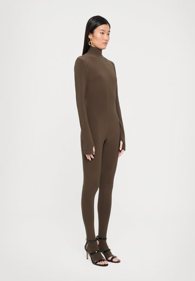 Brown long-sleeve bodysuit with a high neckline, form-fitting design, and thumbholes, paired with black strappy high-heeled sandals.