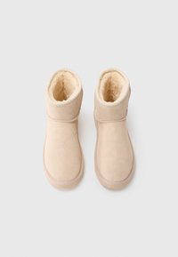 Béžové kotníkové boty vyrobené z měkkého semiše s hřejivým podšívkou, kulatou špičkou a vyšívanými detaily, s nízkým gumovým podešvem.