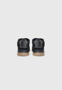 Black sneakers with a textured finish, featuring a smooth grey accent on the heel and a gum rubber sole. Rear view shows padded collar.