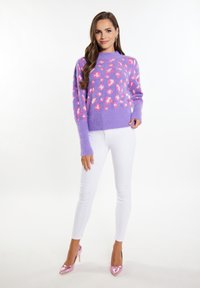 Maglione lavorato a maglia viola con macchie leopardate rosa, caratterizzato da un collo rotondo e maniche lunghe, abbinato a pantaloni bianchi aderenti e tacchi alti rosa.