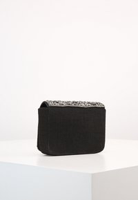 Černá látková taška s texturovaným vrškem zdobeným šedými korálky a ozdobami. Kompaktní obdélníkový tvar, plochý základ, minimalistický design.