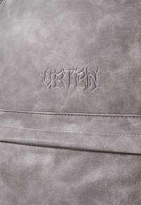 Gray faux leather material with a smooth texture, featuring embossed text detail. The surface shows a subtle sheen and stitching accents.