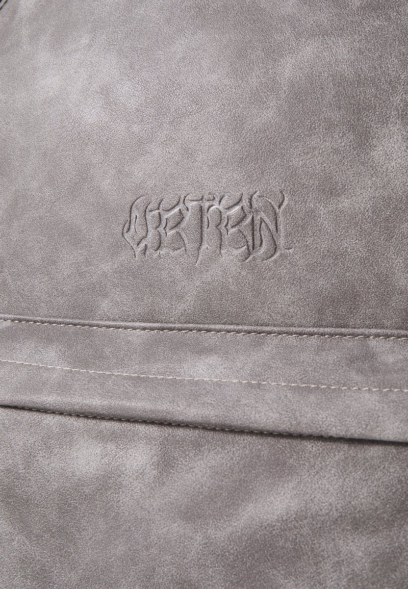 Material de imitación de cuero gris con una textura suave, presentando un detalle de texto en relieve. La superficie muestra un brillo sutil y acentos de costura.