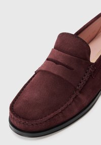 Loafer de camurça vermelho escuro com costura tipo mocassim e sola preta, mostrando detalhes da parte frontal e lateral em fundo branco.