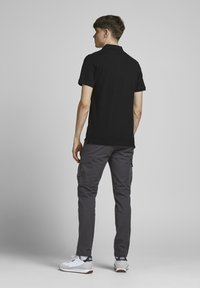 Zwarte polo met korte mouwen, gecombineerd met grijze cargo-broeken. Schoenen zijn wit met grijze accenten. Minimalistisch ontwerp, gladde stofstructuur.