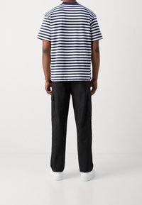 Stribet navy og hvid bomulds T-shirt parret med løse sorte cargo bukser og hvide sneakers, set fra ryggen.