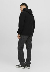 Sudadera negra con una textura gruesa y capucha con cordón, combinada con jeans de mezclilla oscura y zapatillas negras con acentos blancos.