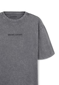 T-shirt grigia oversize realizzata in misto cotone. Presenta una texture consumata e la scritta ricamata "WEST COAST" in grigio scuro sul davanti.