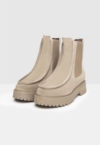 Beige ankelstøvler lavet af ruskind, med elastiske sidepaneler, en tykk sål med en notch-design og afrundede tæer.