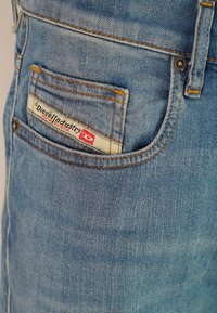 Primo piano di una tasca di jeans blu in denim con cuciture arancioni e un'etichetta Diesel Industry Denim Division.