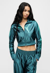 Σμαραγδί σατέν φόρμα με φερμουάρ σε κοντή ζακέτα με λογότυπο και παντελόνι με ελαστική μέση και πλαϊνές τσέπες.