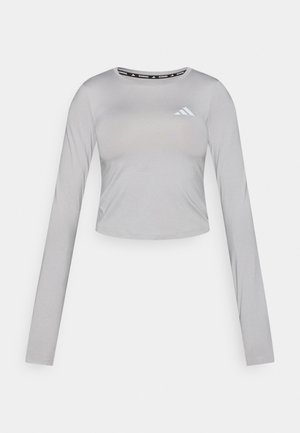 Top crop gri cu mâneci lungi, din material neted, cu decolteu rotund și un logo subtil în zona pieptului stâng.