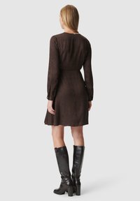 Braun gemustertes Kleid mit langen Ärmeln und einer taillierten Taille, das am Saum sanft ausgestellt ist. Kombiniert mit kniehohen schwarzen Lederstiefeln.
