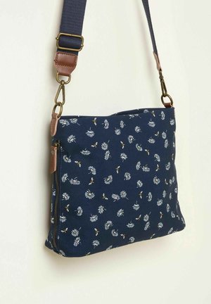 Tumši zila auduma plecu soma ar ziedu rakstu un dzelteniem akcentiem. Ir kabata ar rāvējslēdzēju un auduma regulējams siksna ar brūniem ādas elementiem.