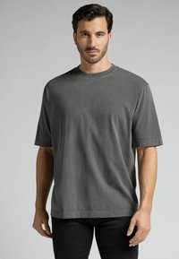 Szara koszulka z krótkim rękawem, wykonana z bawełny, z okrągłym dekoltem i luźnym krojem, o gładkiej fakturze i prostym wykończeniu.