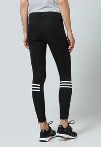 Svarta atletiska tights med vita vertikala ränder vid anklarna, en åtsittande design och dragkedjor vid nederkanten.