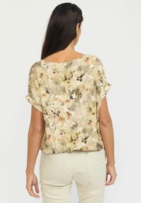 Kortskaft bluse med et let blomstermønster i beige og pastelfarver, der har en løs pasform og en subtil glans. Bagperspektiv vist.