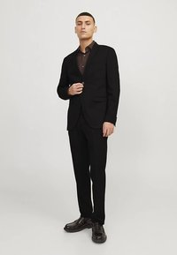 Mustast siidjast kangast ülikond, mis koosneb ühe rinda kinnitatavast bleiserist ja lõigatud pükstest. Kandmiseks sobitatud tume nööbitav särk ja läikivad kingad.