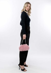 Rosa fluffig handväska med ett silverkedjehandtag, i kombination med en figursydd svart långärmad topp och svarta högmidjade byxor.