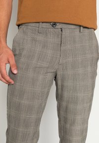 Graue karierte Hose mit einem Schachmuster, ausgestattet mit einem Knopfverschluss, Seitentaschen und einer taillierten Passform, gefertigt aus einem glatten Stoff.