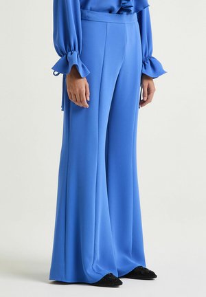 Pantaloni blu a gamba larga realizzati in tessuto liscio, con vita alta e design fluente. Abbinati a scarpe basse nere impreziosite.