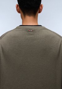 Olivgrüner Pullover mit gerippter Textur und rundem Halsausschnitt. Verfügt über einen kleinen roten, weißen und blauen gestreiften Akzent auf der Rückseite.