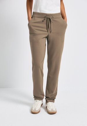 Khaki jogger pants made of soft fabric, featuring a drawstring waistband, side pockets, and tapered legs, paired with white sneakers.