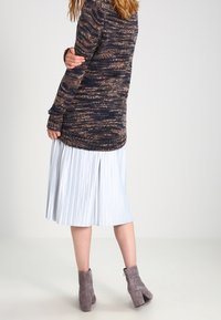 Sweter robiony na drutach o wielokolorowym wzorze w ciemnych odcieniach, w połączeniu z plisowaną jasnoniebieską spódnicą i szarymi botkami za kostkę.