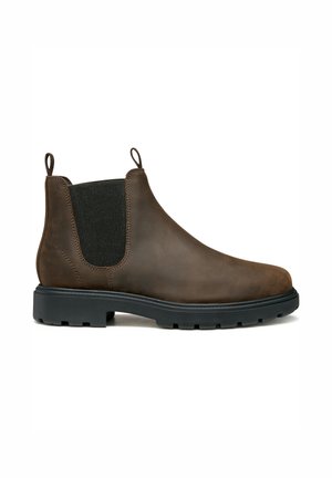 Bota Chelsea de cuero marrón con paneles elásticos en los laterales, una lengüeta y una suela de goma negra con un agarre texturizado para tracción.