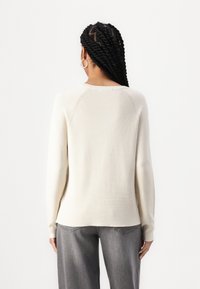 Beige kötött pulcsi hosszú ujjakkal, kerek nyakkivágással és enyhén bő szabással. Texturált anyag, látható varrásrészletekkel.