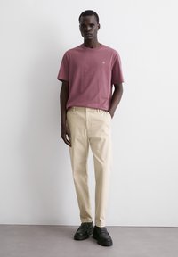 Camiseta de manga corta y cuello redondo en rosa empolvado, combinada con pantalones beige ajustados. El calzado son mocasines negros con suela gruesa.