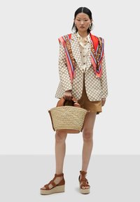 Beige mönstrad blazern, krämfärgad blus, bruna shorts, vävd halmhandväska med bruna läderdetaljer och bruna kilklacksandaler.